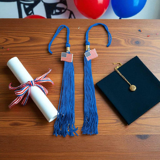Rocky Mountain Balfour blue graduation tassels with USA flag charms next to a diploma and graduation cap